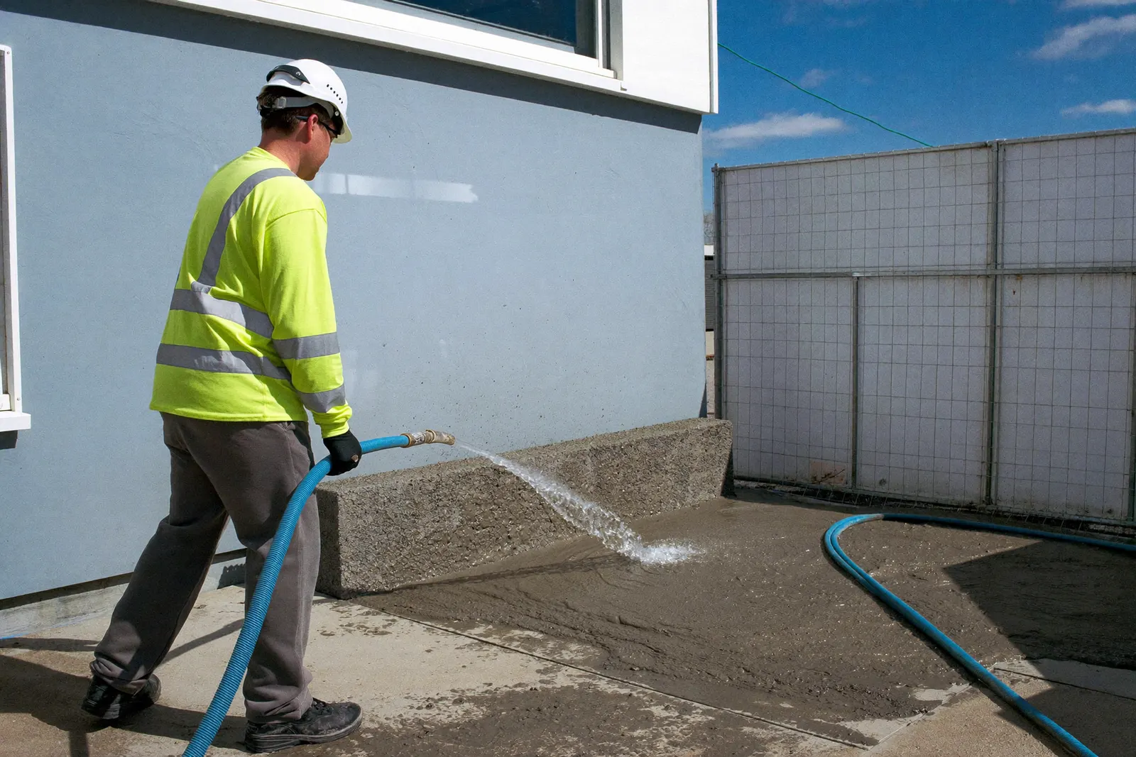 Australian labourer in long-sleeve high-vis and hard hat working wet concrete on site