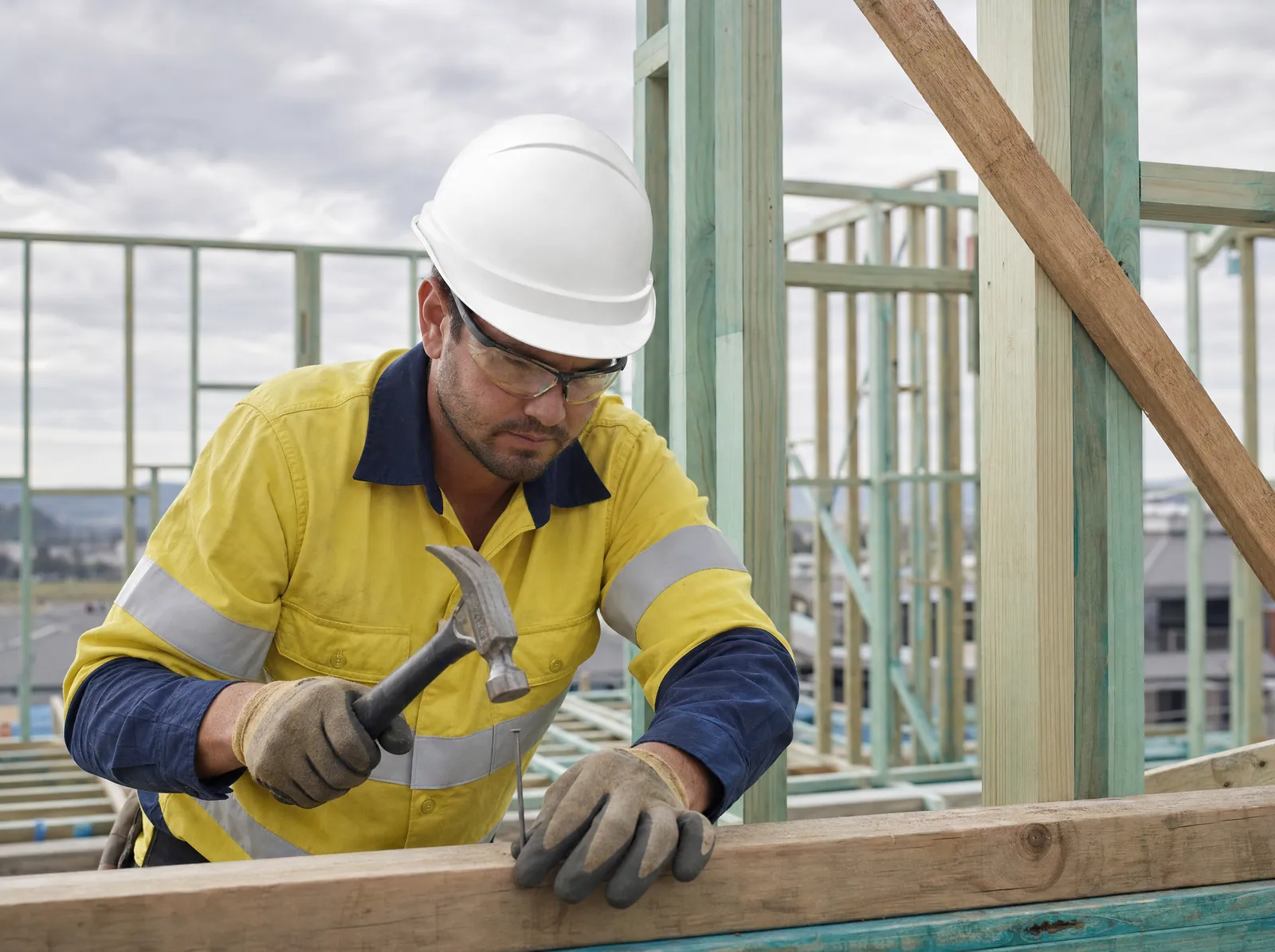 Australian carpenter in high-vis and hard hat hammering timber framing on site